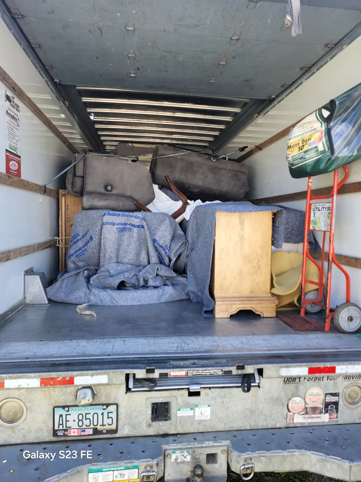 Moving pads covering household furniture with tie-down straps visible across the load in a Rowann job